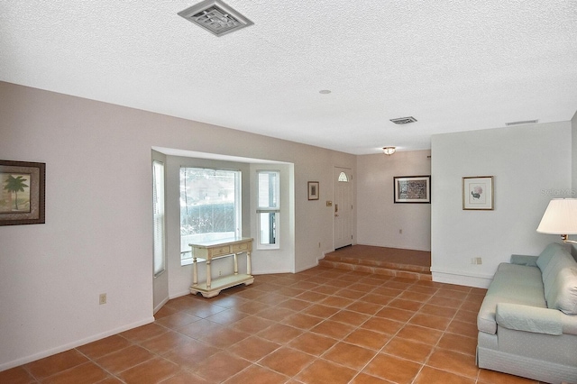 unfurnished living room with a textured ceiling, light tile patterned floors, visible vents, and baseboards