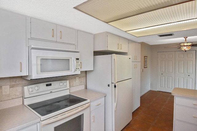 kitchen with tasteful backsplash, dark tile patterned floors, white cabinets, and white appliances