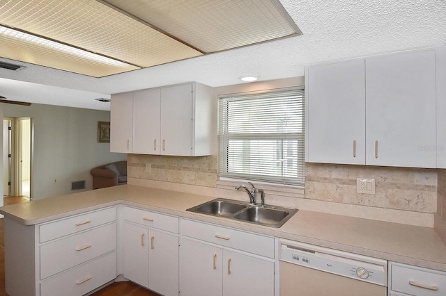 kitchen with light countertops, visible vents, white dishwasher, a sink, and a peninsula