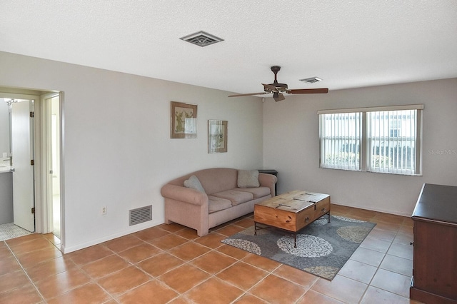 living room with a textured ceiling, light tile patterned flooring, visible vents, and a ceiling fan