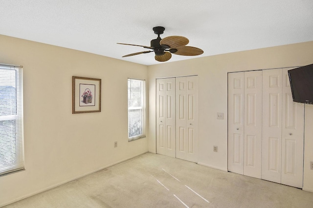 unfurnished bedroom with multiple closets, light colored carpet, ceiling fan, and a textured ceiling