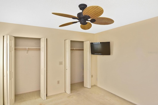 unfurnished bedroom featuring ceiling fan, light colored carpet, and multiple closets