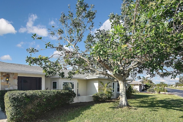 view of front of home with an attached garage, stone siding, driveway, stucco siding, and a front lawn