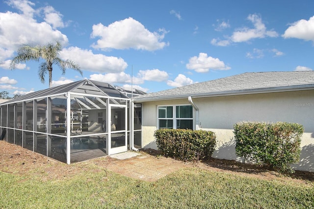 back of house with a lanai, roof with shingles, and stucco siding