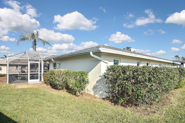 back of house with glass enclosure, a yard, and stucco siding