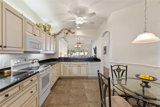 kitchen with white appliances, dark countertops, a sink, and cream cabinetry