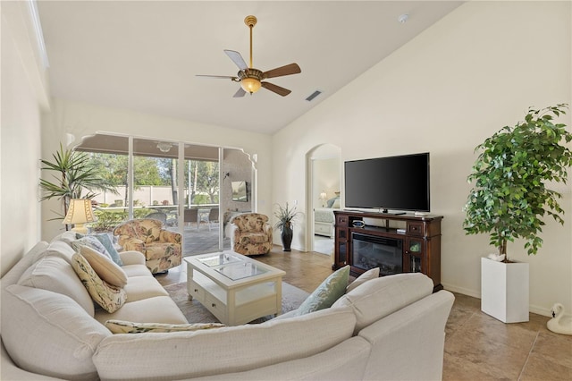 living area featuring visible vents, a ceiling fan, a glass covered fireplace, high vaulted ceiling, and baseboards