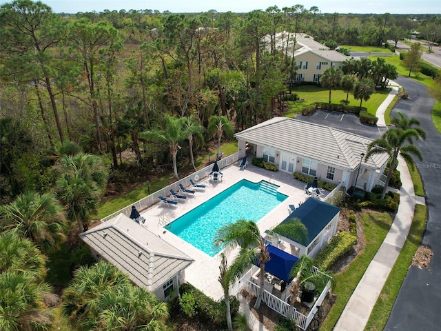 community pool featuring fence, a wooded view, and a patio