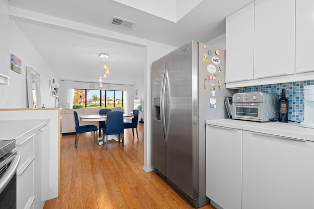 kitchen with light hardwood / wood-style flooring, appliances with stainless steel finishes, white cabinetry, hanging light fixtures, and tasteful backsplash