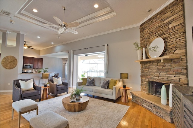 living room featuring a raised ceiling, ceiling fan, light wood-type flooring, and a fireplace