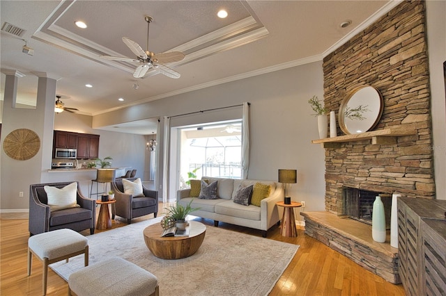 living room featuring ceiling fan, a stone fireplace, light wood-type flooring, and a tray ceiling