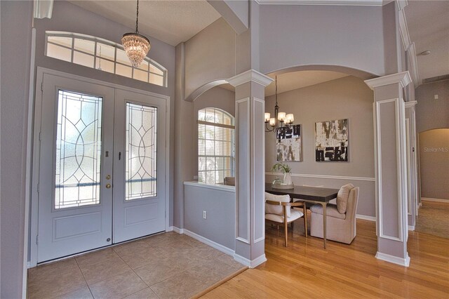 foyer entrance featuring an inviting chandelier, light hardwood / wood-style flooring, french doors, and ornate columns