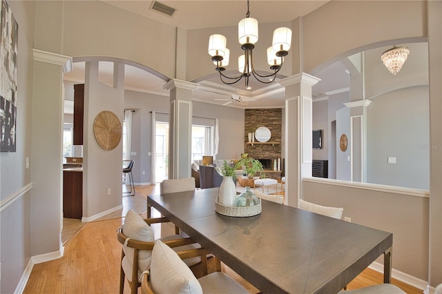 dining area featuring an inviting chandelier, a fireplace, light hardwood / wood-style floors, and ornate columns