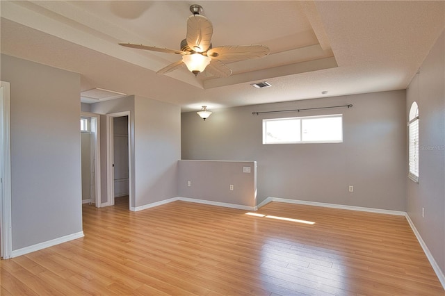 unfurnished room featuring ceiling fan, a raised ceiling, a textured ceiling, and light wood-type flooring