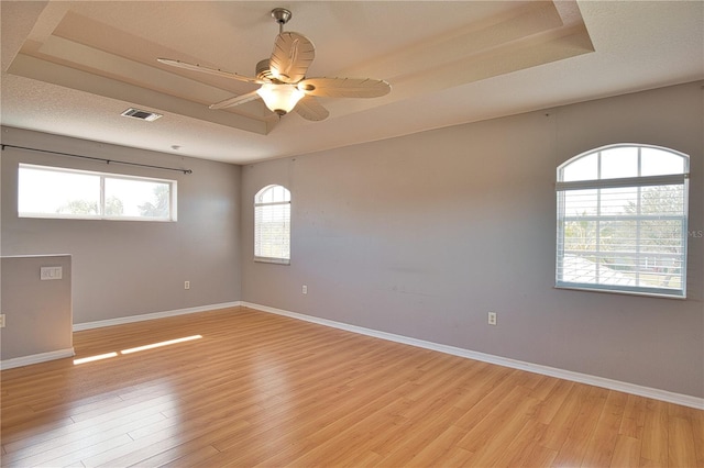 empty room featuring a textured ceiling, light hardwood / wood-style flooring, a raised ceiling, and ceiling fan