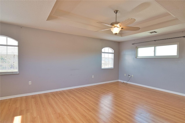 spare room featuring a textured ceiling, light hardwood / wood-style floors, a raised ceiling, and ceiling fan