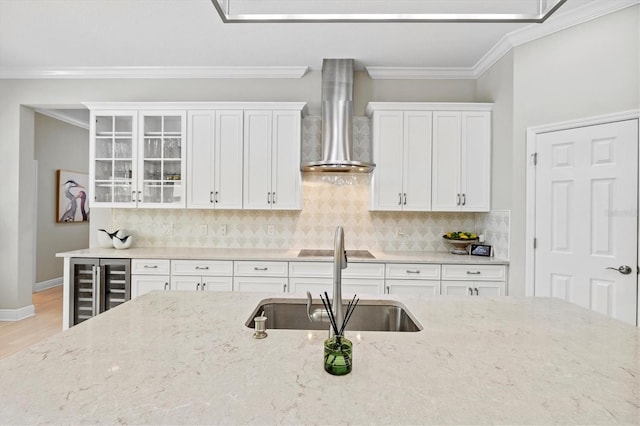 kitchen featuring decorative backsplash, ornamental molding, white cabinets, a sink, and wall chimney exhaust hood