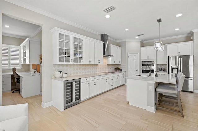 kitchen with stainless steel appliances, visible vents, a sink, wall chimney range hood, and beverage cooler