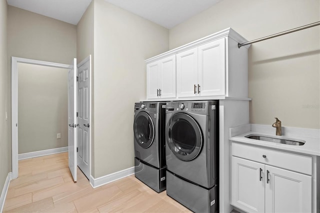 laundry room featuring washing machine and clothes dryer, cabinet space, light wood-style floors, a sink, and baseboards