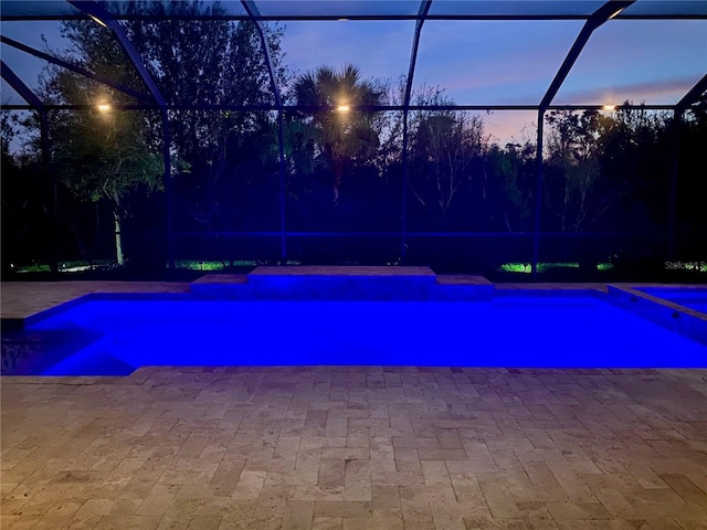 pool at dusk featuring a pool with connected hot tub, a lanai, and a patio