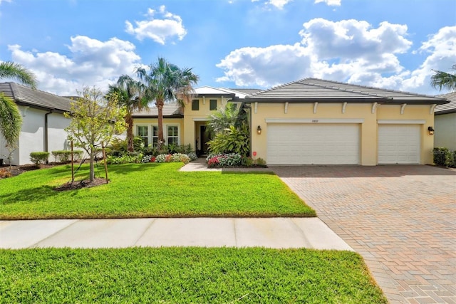 view of front of property featuring a garage, a tile roof, decorative driveway, a front lawn, and stucco siding