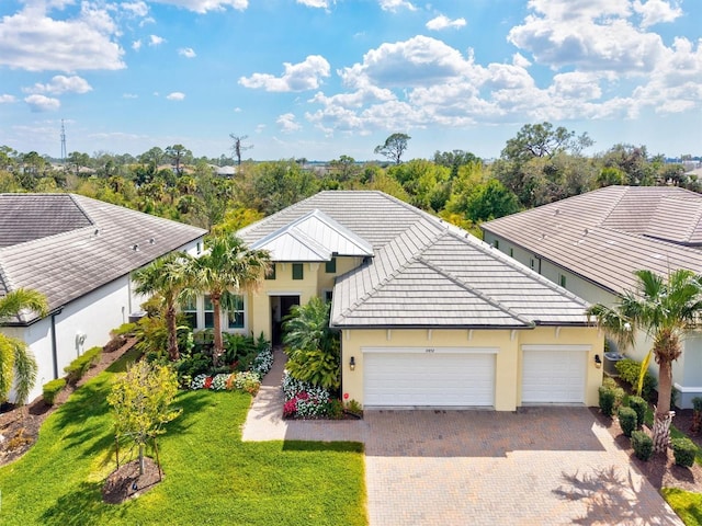 view of front of home featuring a tile roof, an attached garage, decorative driveway, a front yard, and stucco siding