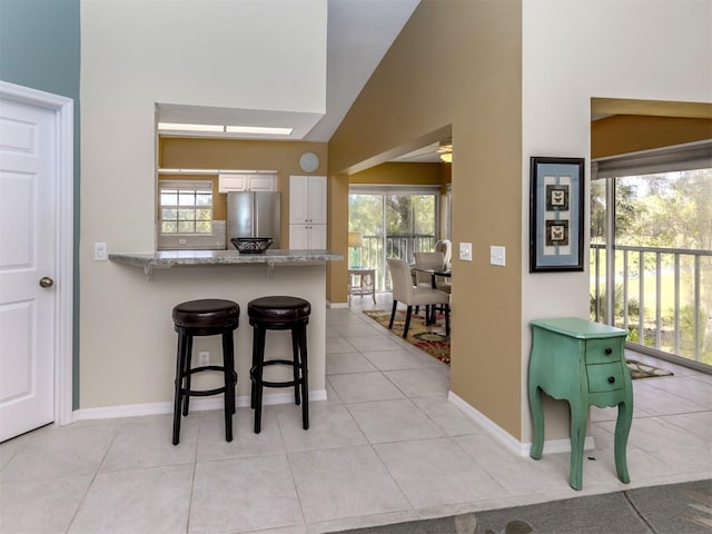 kitchen featuring a breakfast bar, a wealth of natural light, white cabinets, and stainless steel refrigerator