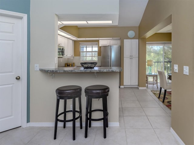 kitchen featuring a breakfast bar, white cabinetry, light stone counters, kitchen peninsula, and stainless steel appliances