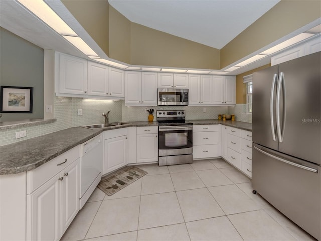 kitchen with lofted ceiling, sink, light tile patterned floors, stainless steel appliances, and white cabinets