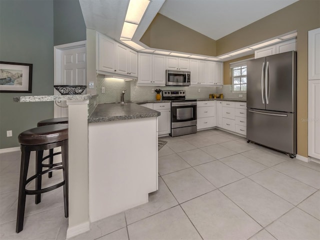 kitchen with white cabinetry, stainless steel appliances, a kitchen breakfast bar, tasteful backsplash, and kitchen peninsula