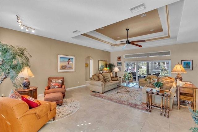 tiled living room with ceiling fan and a raised ceiling