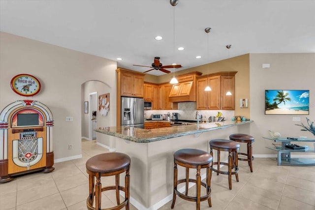 kitchen featuring appliances with stainless steel finishes, dark stone countertops, decorative backsplash, decorative light fixtures, and kitchen peninsula