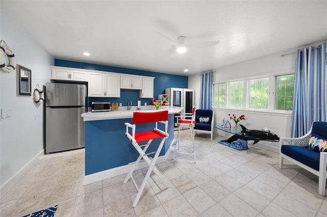 kitchen with an island with sink, white cabinetry, stainless steel appliances, ceiling fan, and a kitchen bar