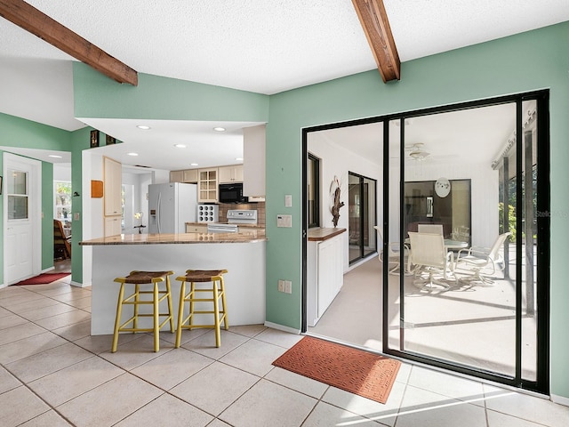 kitchen with light tile patterned floors, white appliances, vaulted ceiling with beams, white cabinets, and kitchen peninsula