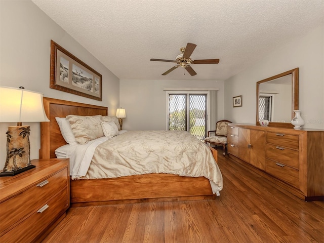 bedroom with ceiling fan, hardwood / wood-style floors, access to exterior, and a textured ceiling