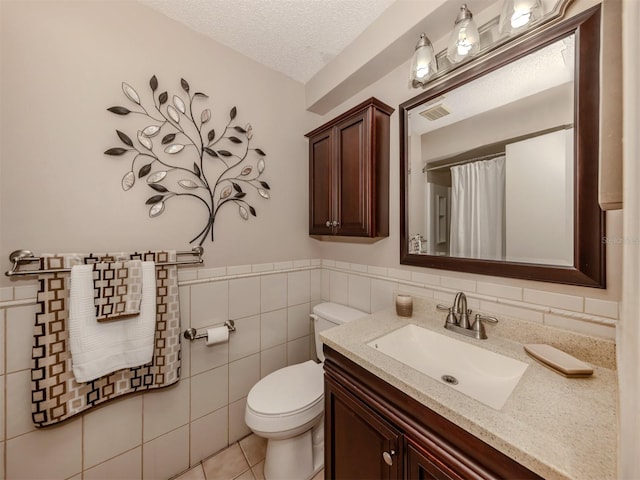 bathroom with toilet, a textured ceiling, tile walls, vanity, and tile patterned flooring