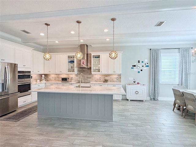 kitchen with white cabinetry, wall chimney range hood, stainless steel appliances, and an island with sink