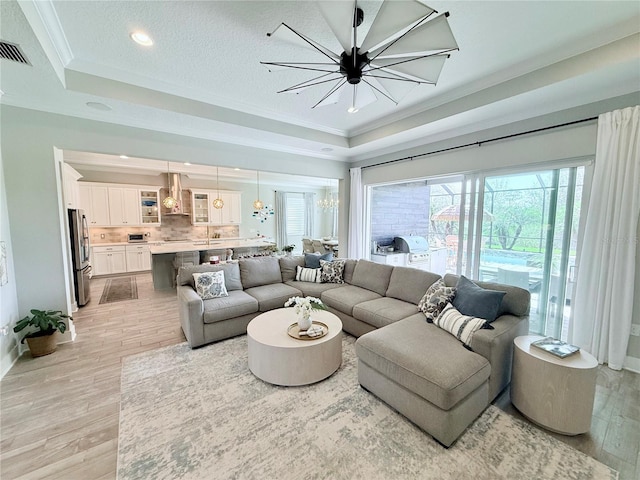 living room with a raised ceiling, crown molding, and an inviting chandelier