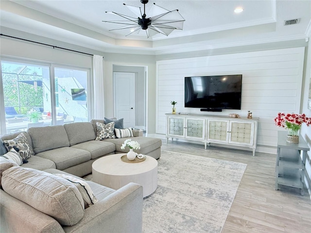 living room with a chandelier, ornamental molding, a raised ceiling, and light hardwood / wood-style flooring