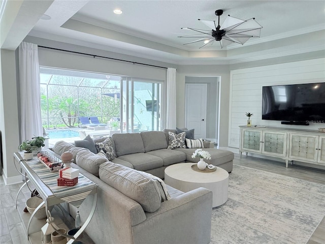 living room featuring ornamental molding, a raised ceiling, and light wood-type flooring