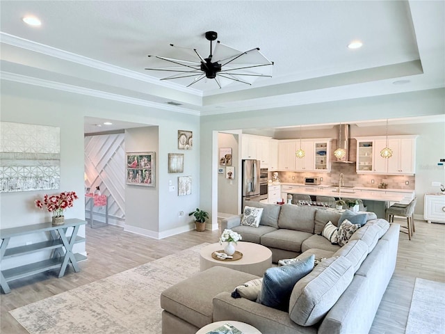 living room with crown molding, a raised ceiling, and light wood-type flooring