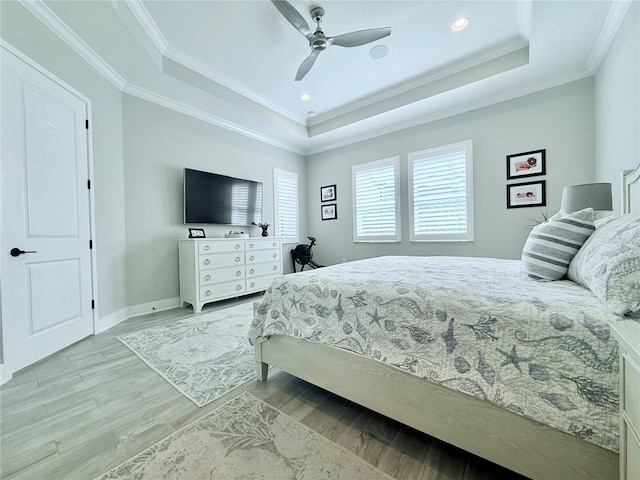 bedroom featuring ceiling fan, ornamental molding, a tray ceiling, and light wood-type flooring