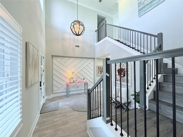 stairway featuring wood-type flooring, ornamental molding, a chandelier, and a towering ceiling