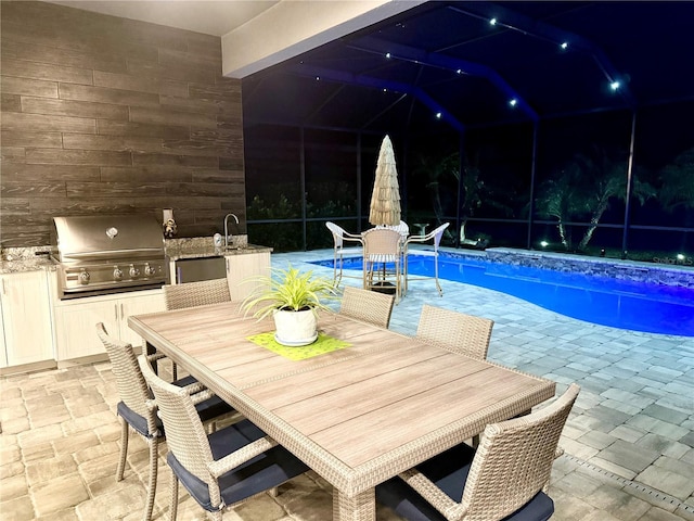 pool at night featuring an outdoor kitchen, area for grilling, and a patio area