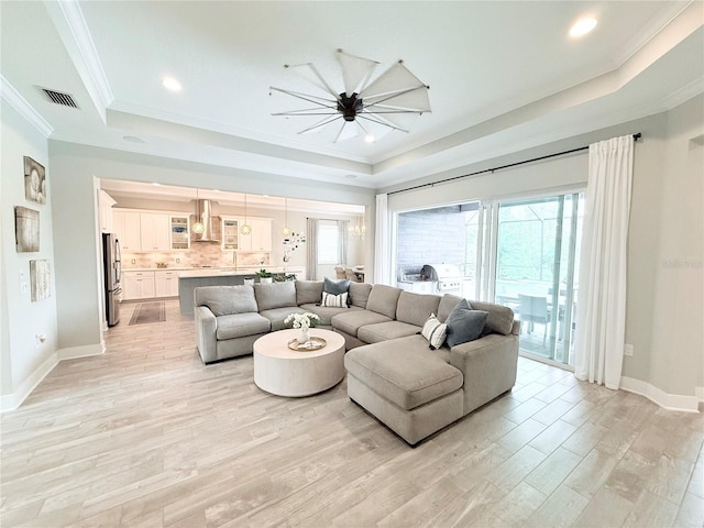 living area with light wood-type flooring, a raised ceiling, baseboards, and crown molding