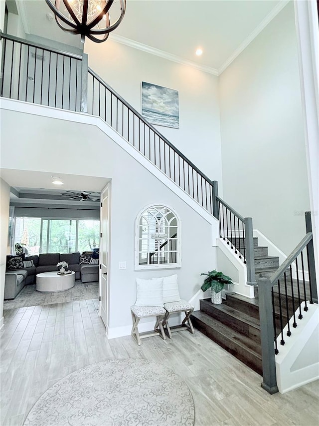 stairway with wood finished floors, baseboards, a high ceiling, ceiling fan, and crown molding