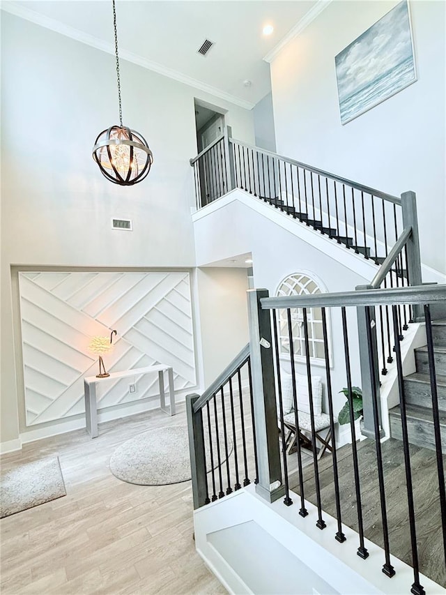 staircase featuring visible vents, wood finished floors, crown molding, a chandelier, and a towering ceiling