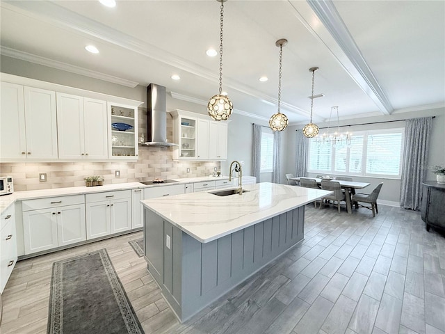 kitchen featuring wood finish floors, a sink, an inviting chandelier, wall chimney exhaust hood, and black electric cooktop