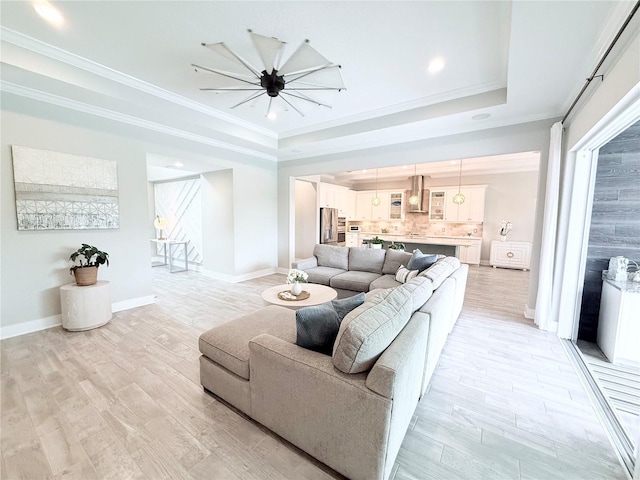 living area with baseboards, light wood-type flooring, crown molding, and a tray ceiling