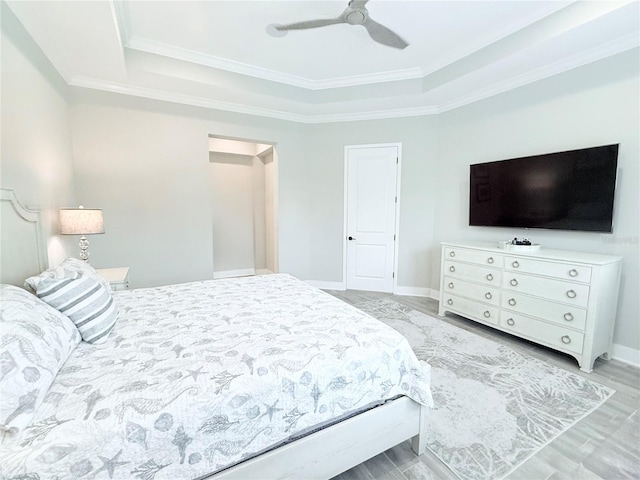 bedroom featuring light wood-type flooring, baseboards, a raised ceiling, and ornamental molding